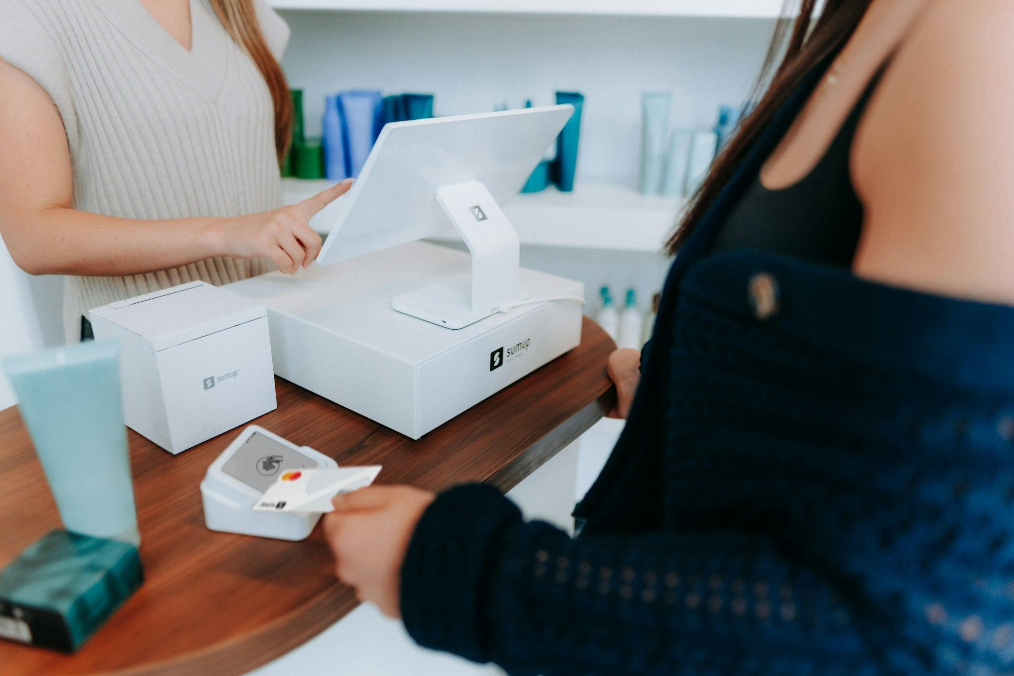 A full SumUp till setup on a shop counter: till screen, receipt printer and card reader taking a payment